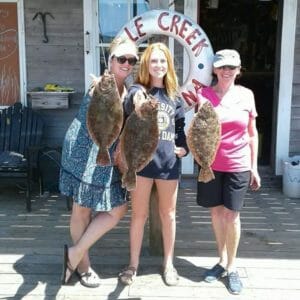 Three women holding their founder catch on dock at Whale Creek Marina